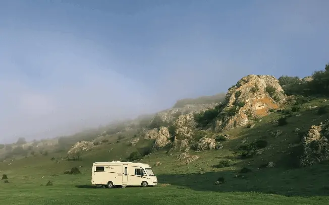 An RV beside a green hill and blue sky