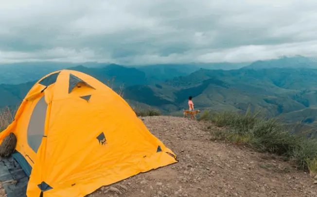 Orange tent with woman and dog standing on mountain