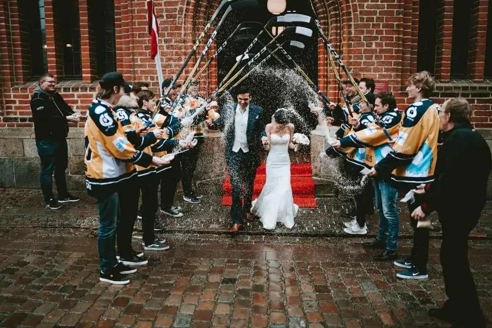 Hockey players lifting their sticks as bride and groom walk under them
