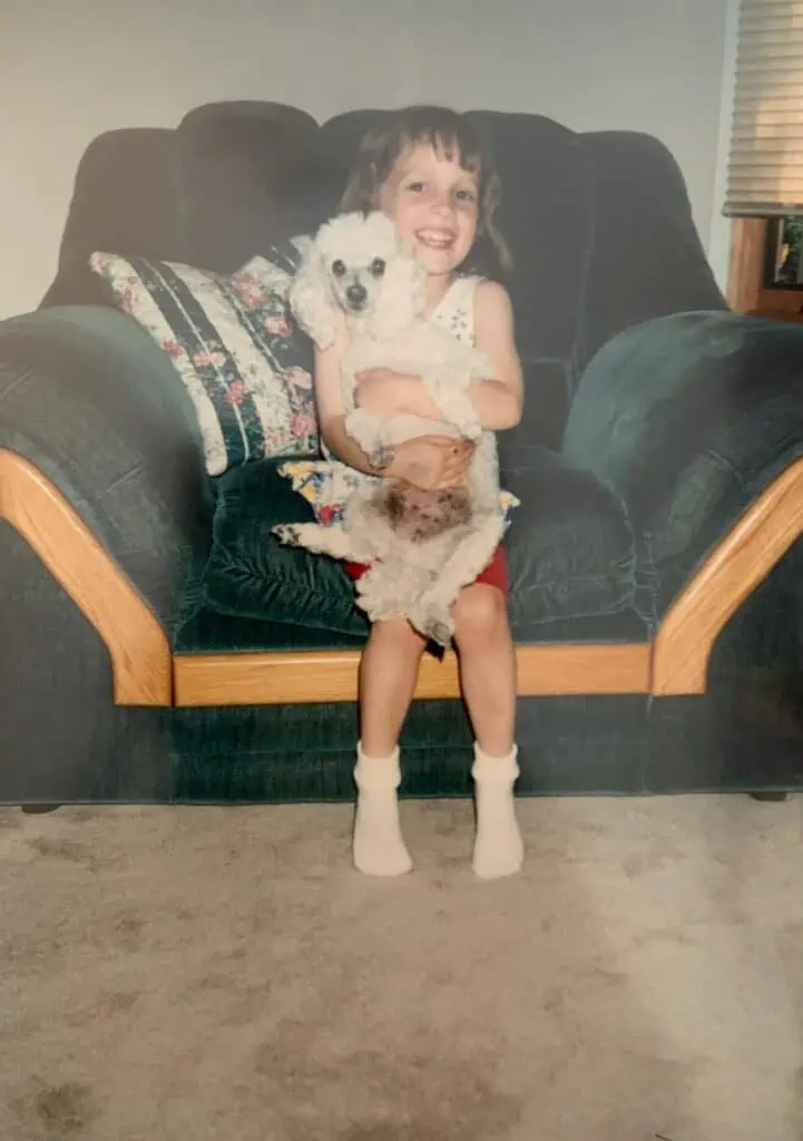 A little girl holding a toy poodle dog while sitting on a couch.