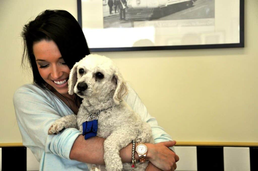 A woman with brown hair smiling and holding a small white dog.